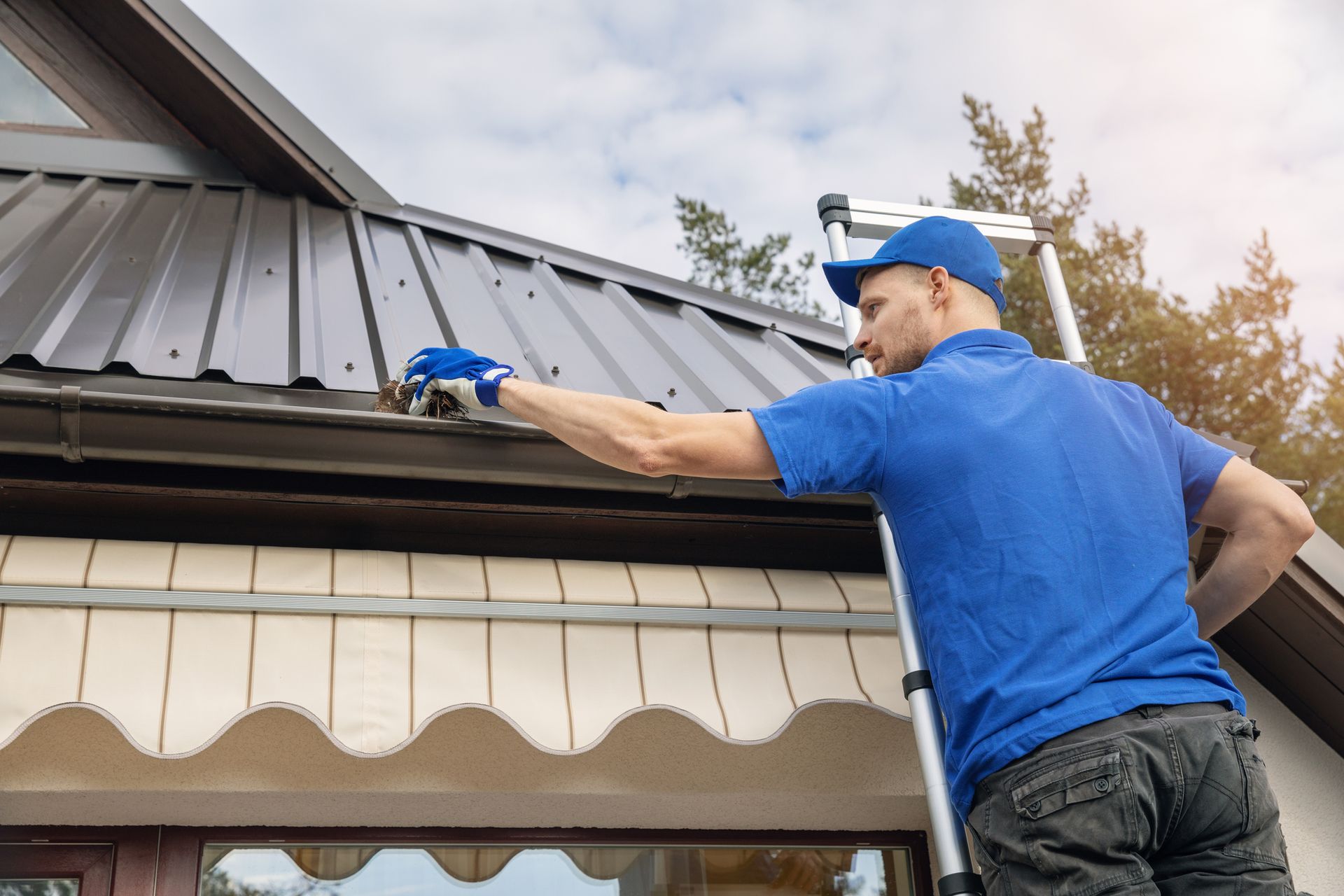 A man is standing on a ladder working on the roof of a house.