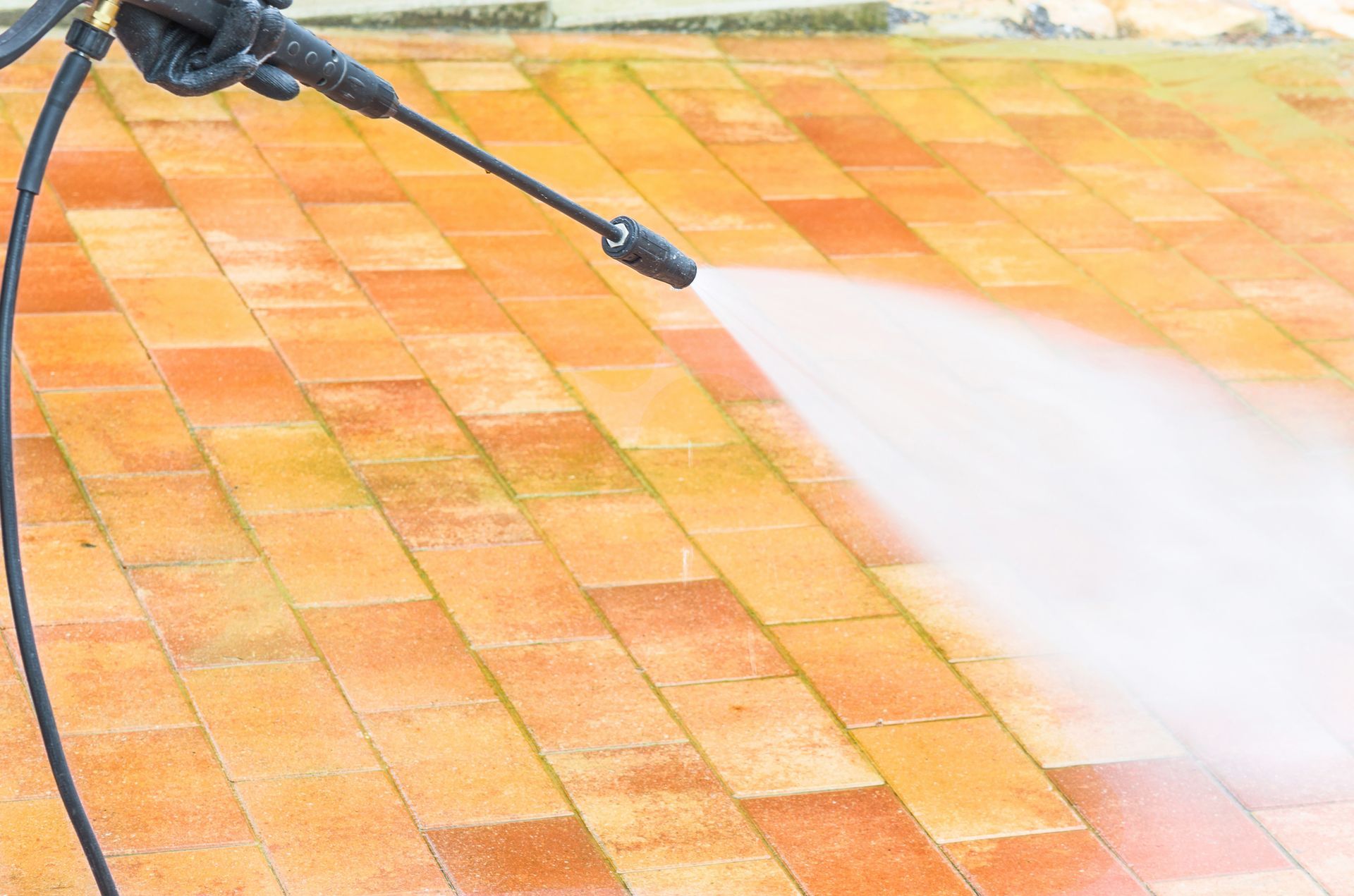 A person is using a high pressure washer to clean a brick walkway.