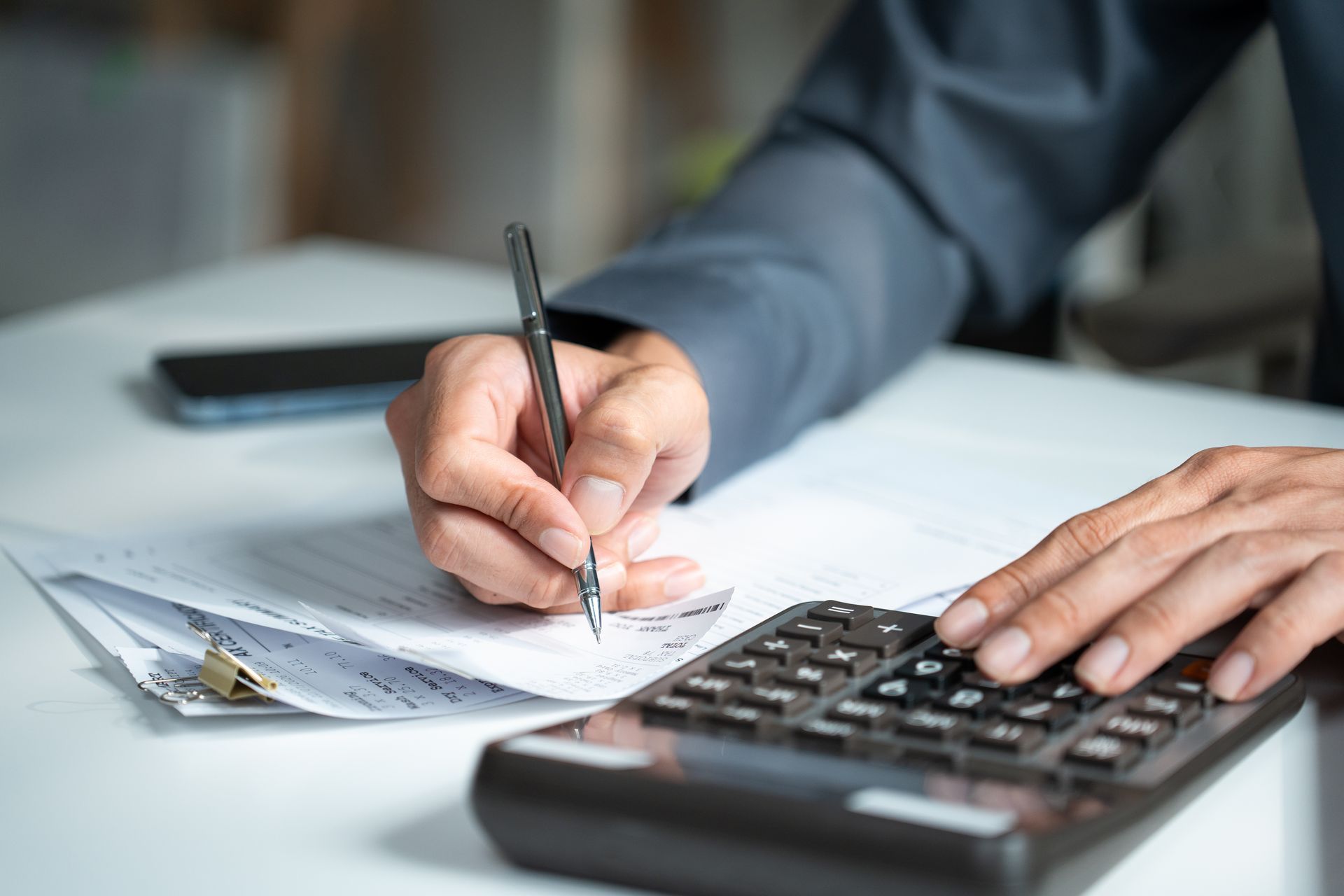 Hand writing on a paper invoice beside a calculator on a desk
