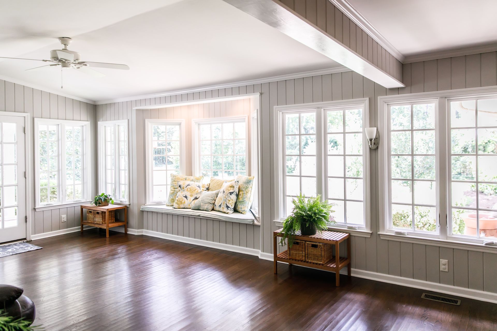 A bright sunroom with large multi-pane windows, a bay window seat, and wood-plank walls A bright sunroom with large multi-pane windows, a bay window seat, and wood-plank walls