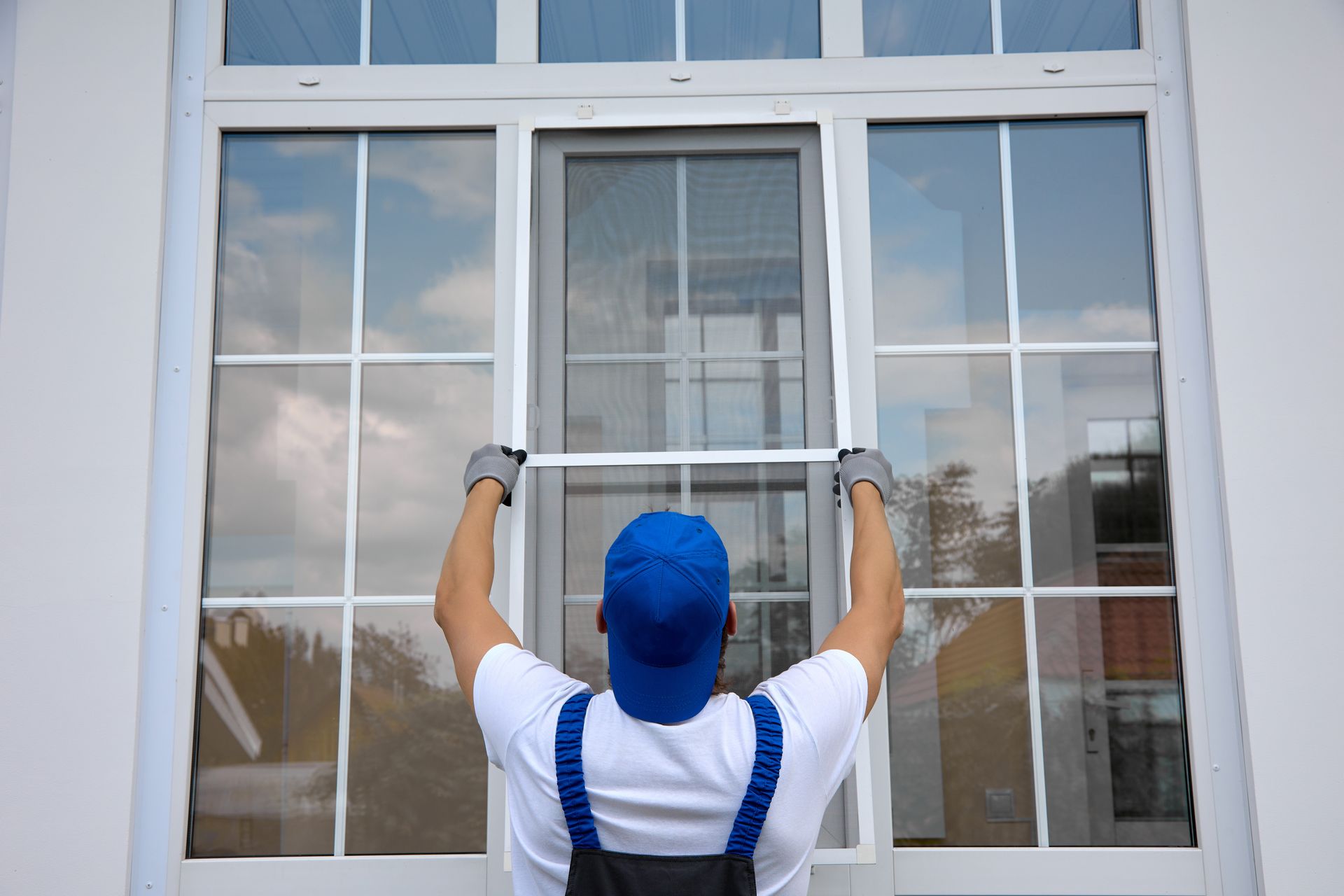A worker installing a window screen on a large glass window with white frames. A worker installing a window screen on a large glass window with white frames.