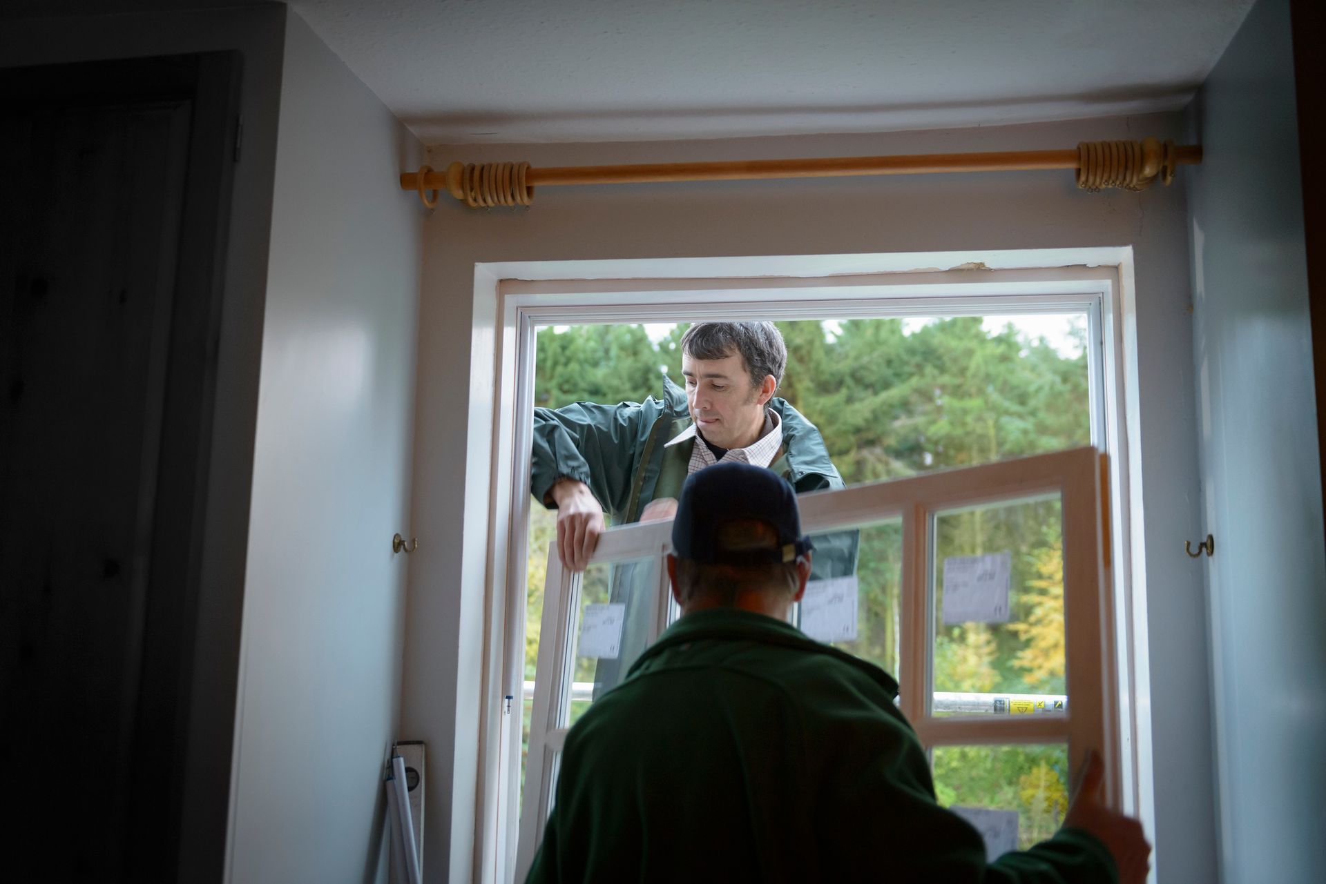 Two contractors performing window installation in residential home with outdoor view. Two contractors performing window installation in residential home with outdoor view.
