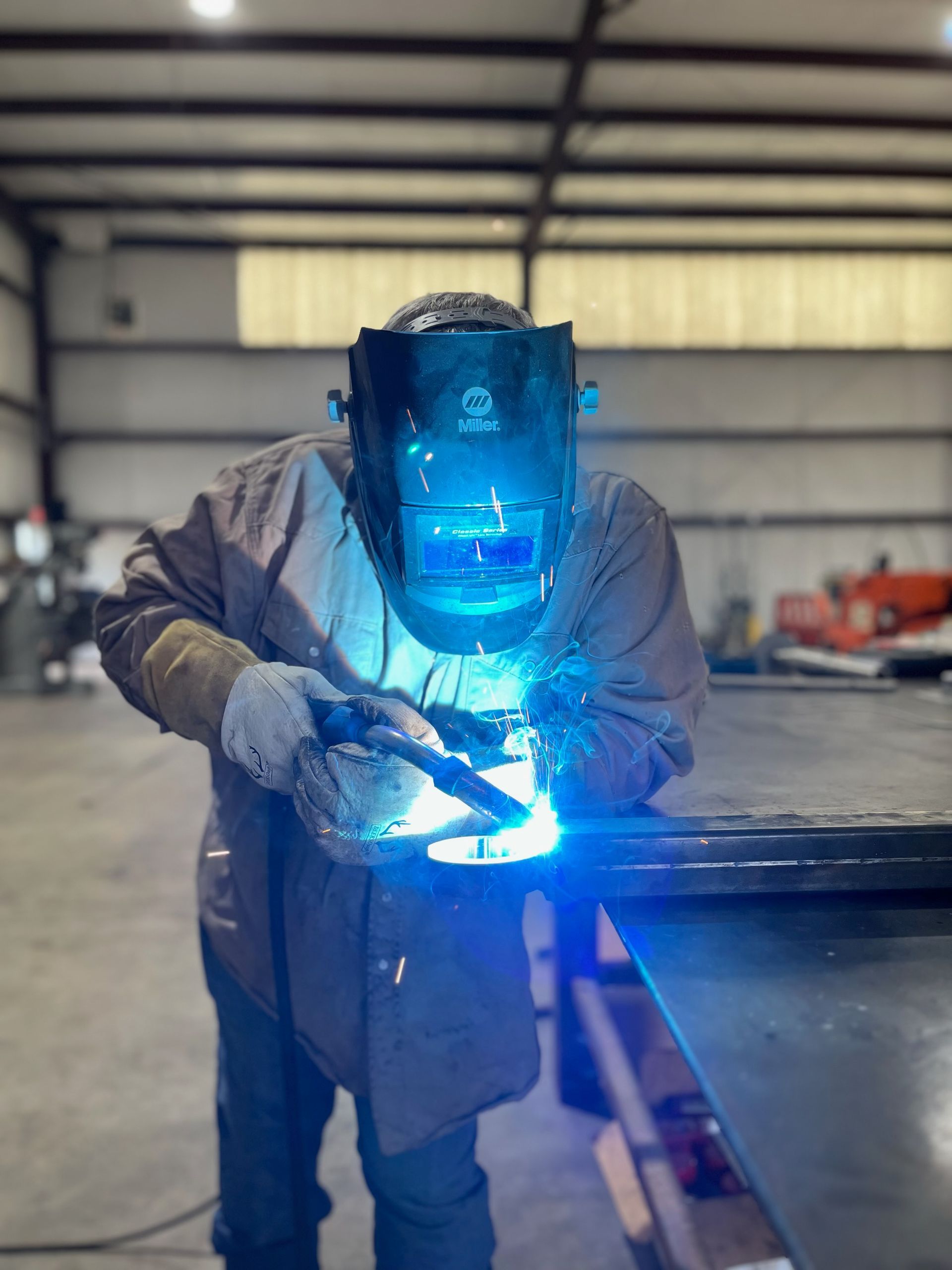 Welder in protective gear working on a metal beam, bright blue arc light in an industrial workshop