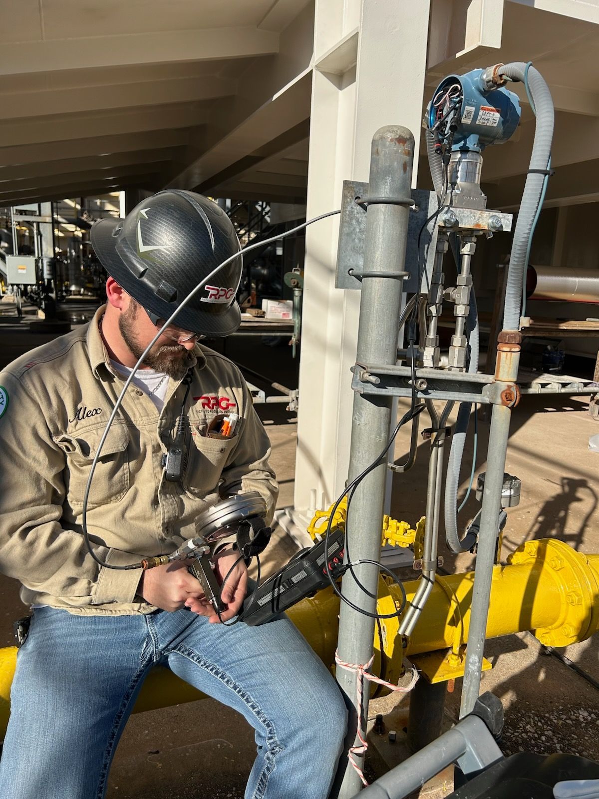 Worker in hard hat inspecting equipment beside a yellow industrial pipe system.