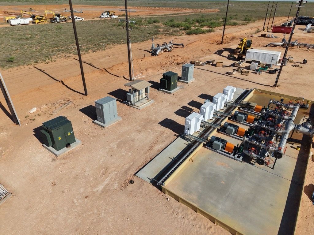 Aerial view of outdoor electrical equipment and transformers on a dirt construction site.