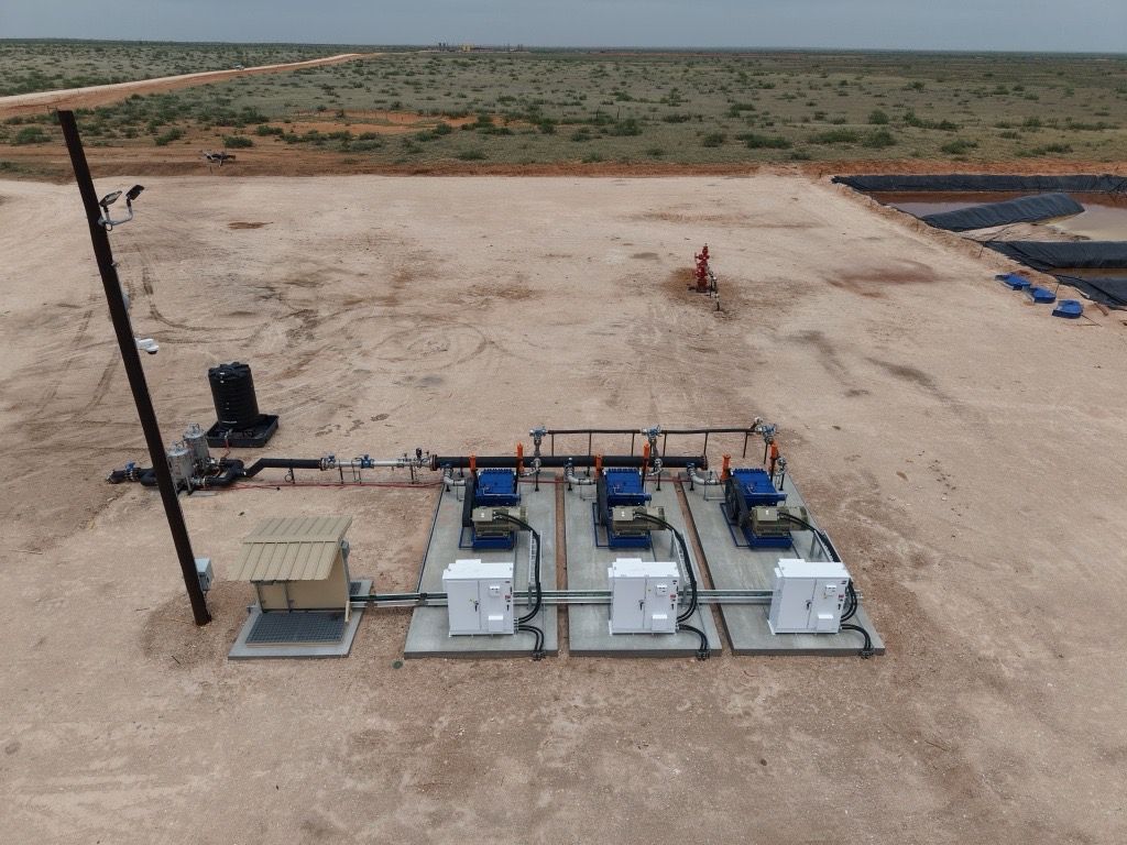 Solar equipment on a concrete platform in a barren landscape, with three white machines and a tall pole.