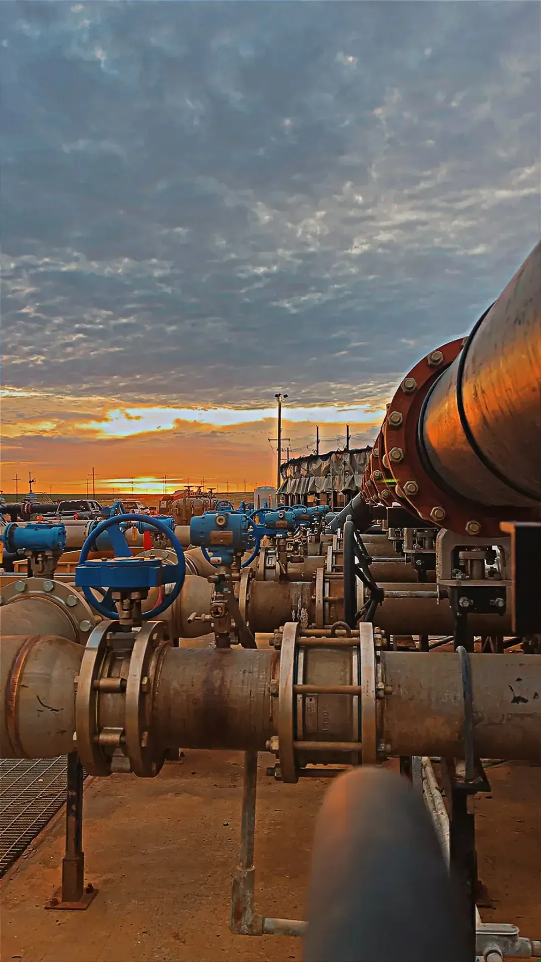 Industrial pipes and blue valves at sunset under a cloudy sky