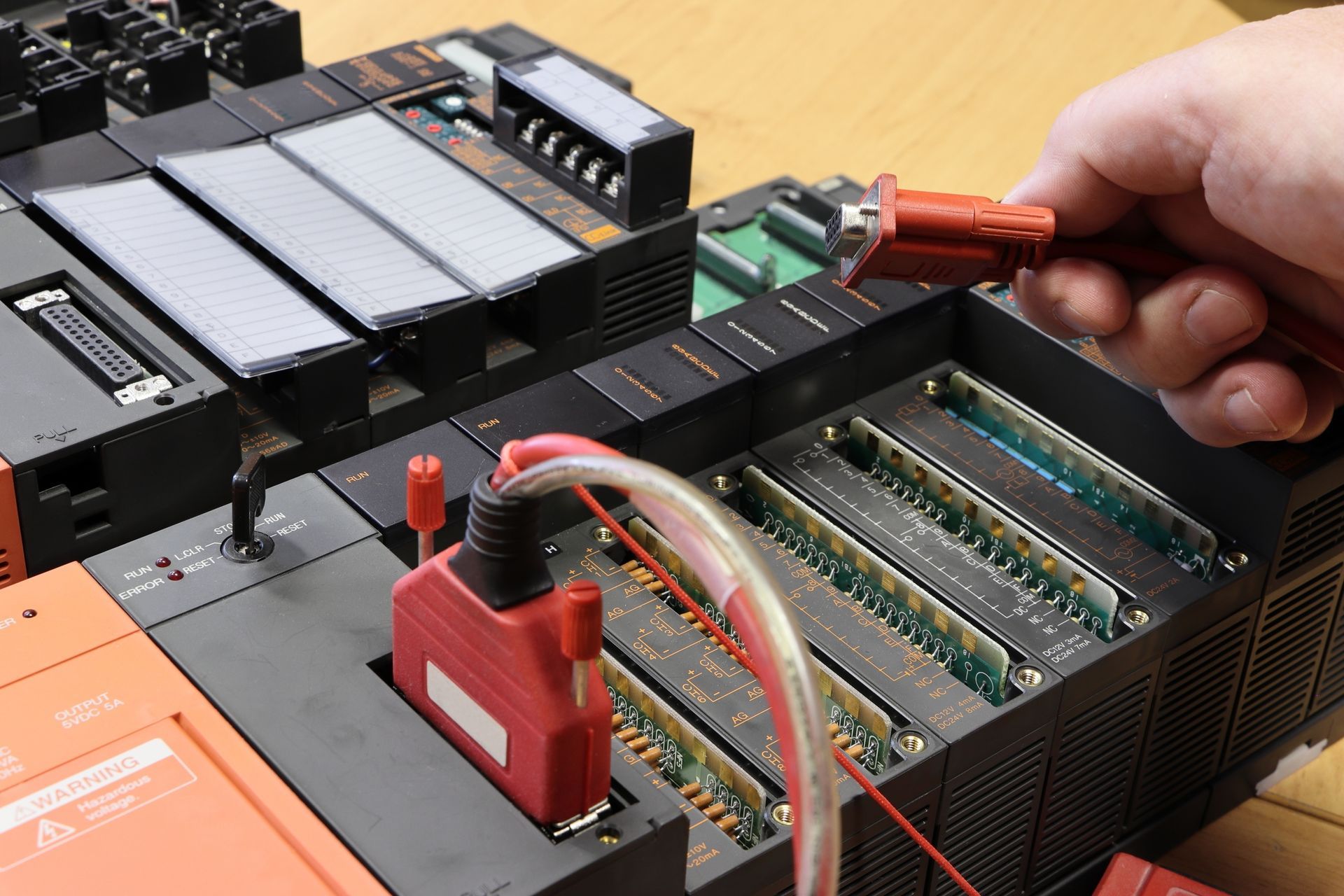 Hand using a probe on an open electronic circuit board with cables and components