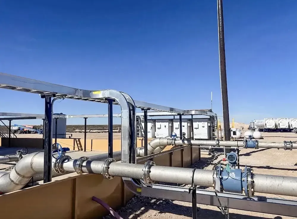Industrial pipes and valves in a desert facility under a clear blue sky