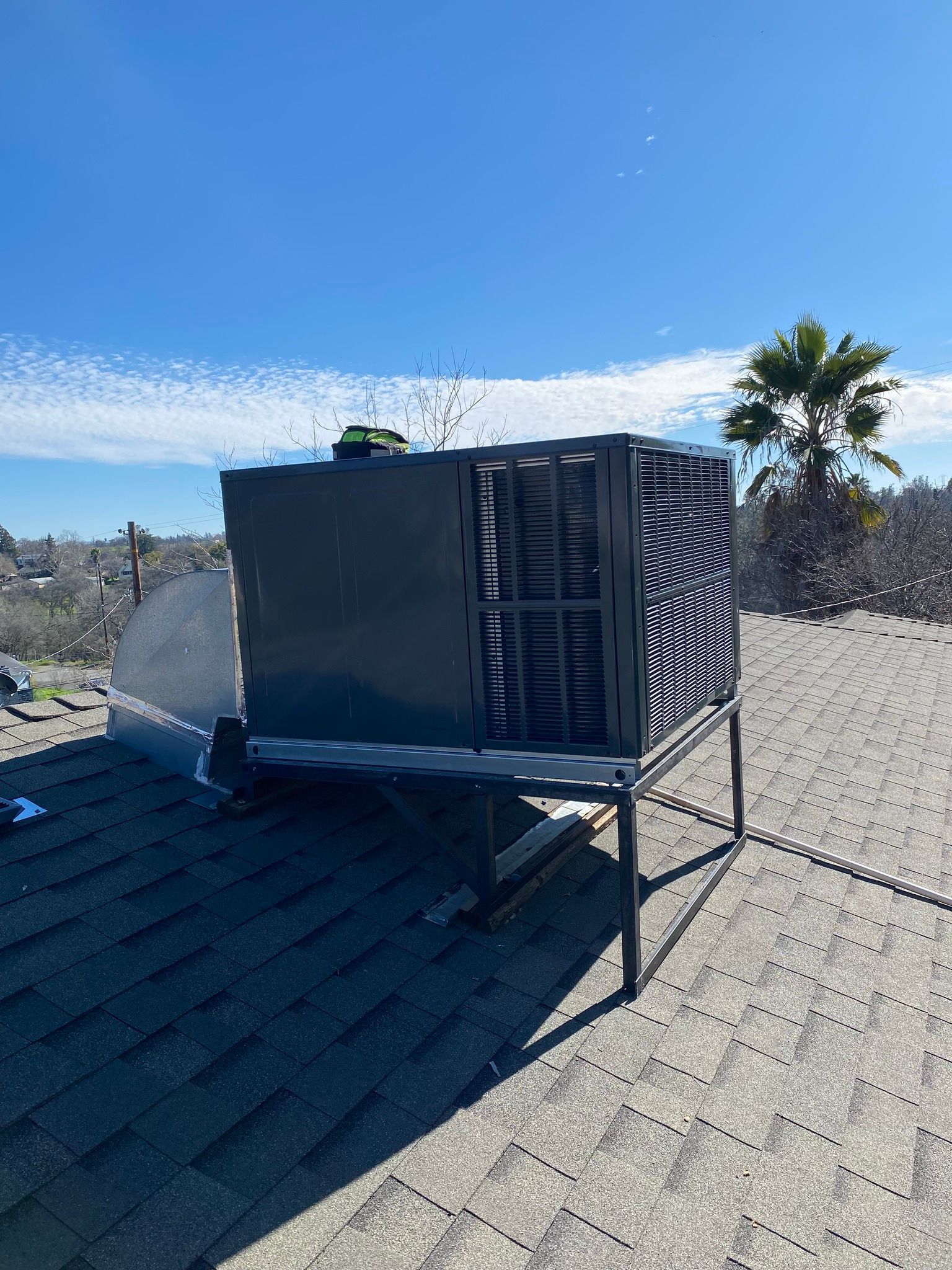 Large black HVAC unit on a rooftop under a clear blue sky, with a palm tree in the background.