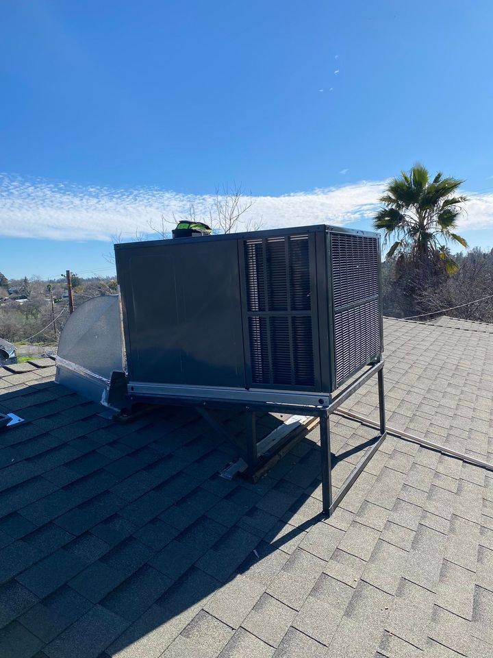 Black rooftop HVAC unit on a shingled roof under a clear blue sky.