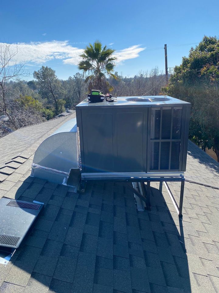Large rooftop HVAC unit on a sloped shingle roof under a bright blue sky