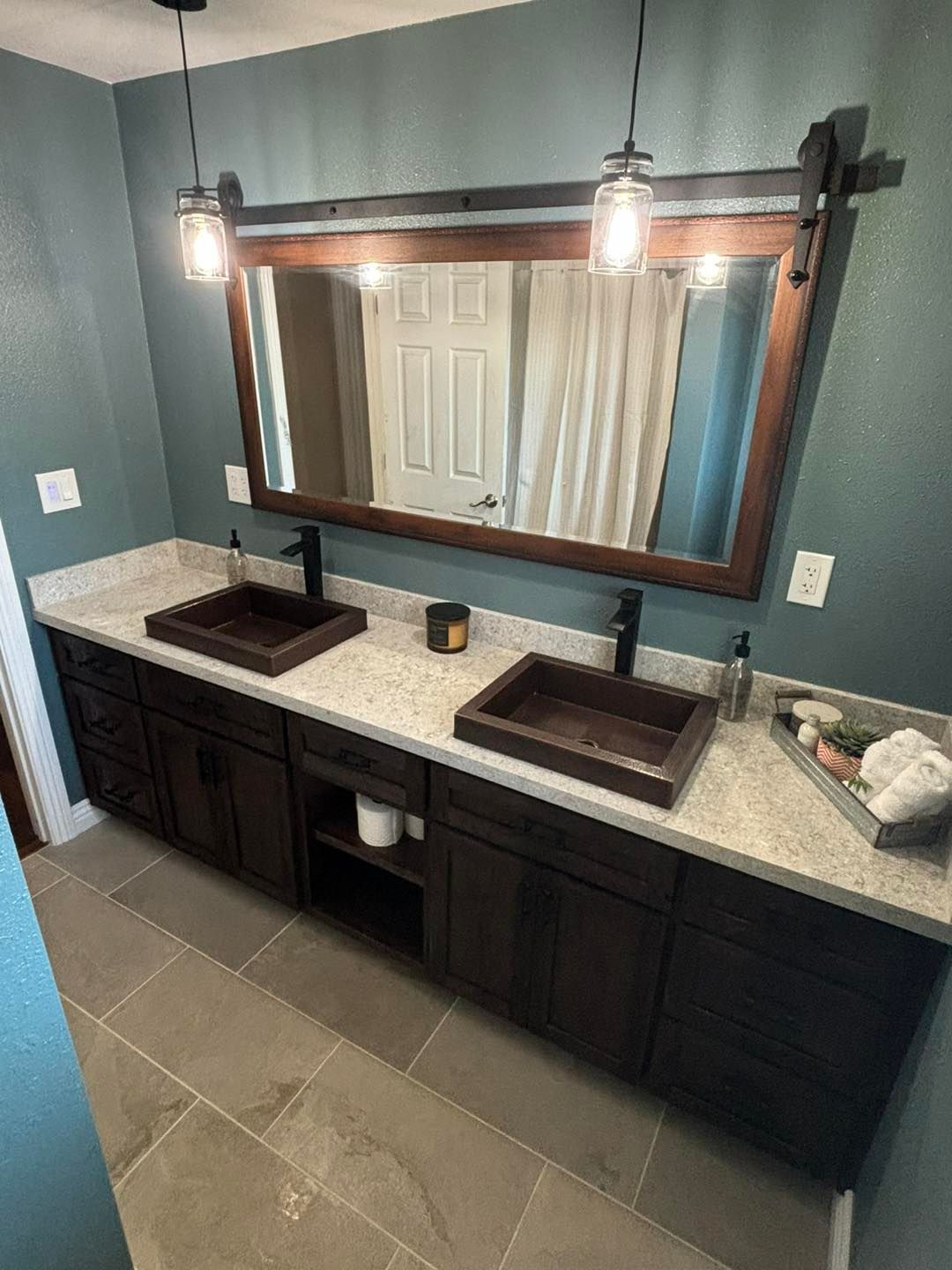 Modern bathroom vanity with double sinks, large mirror, dark cabinets, and blue-green walls