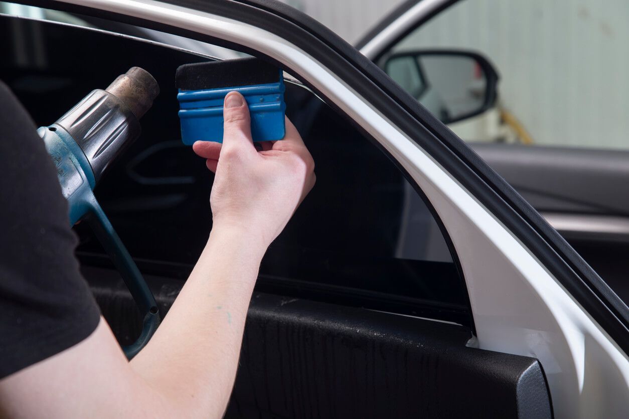 A man works on a car window, demonstrating a step in the window tint removal process.