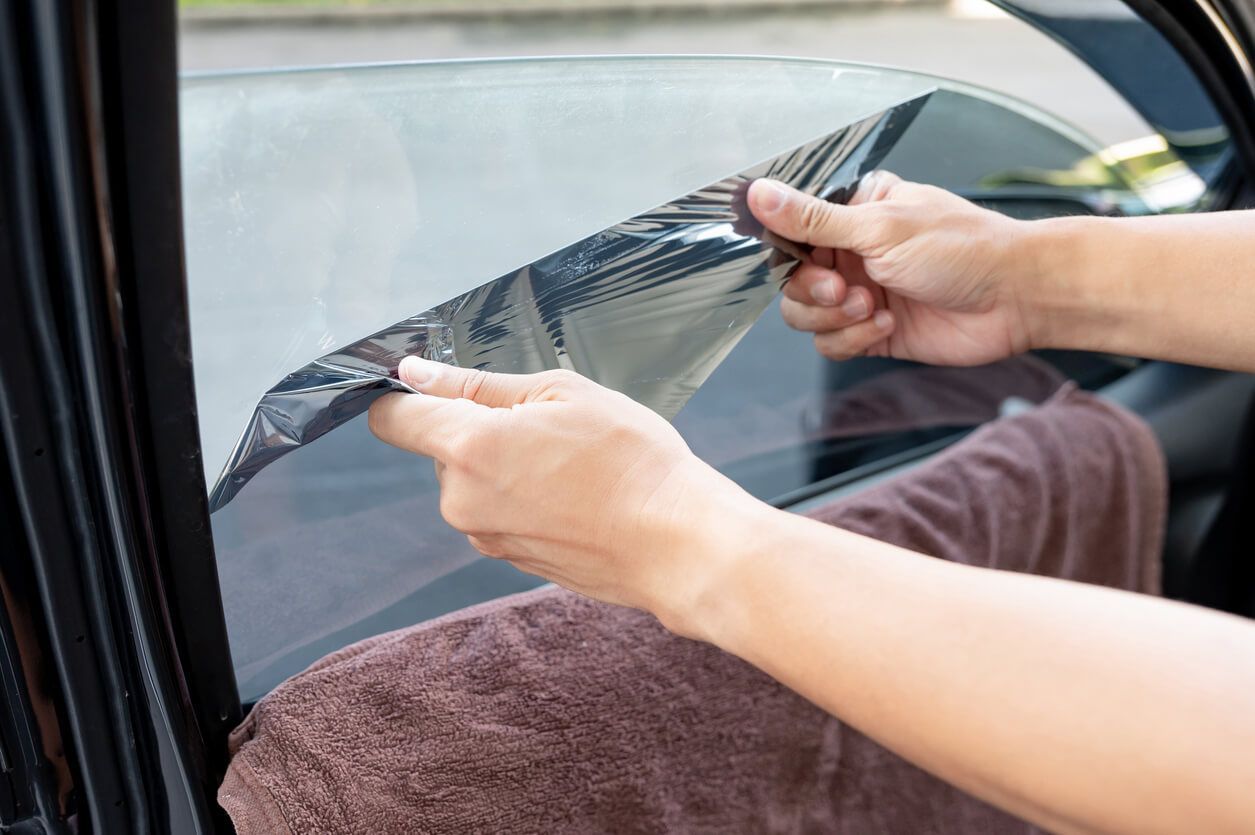 A man works on a car window, demonstrating a step in the window tint removal process.
