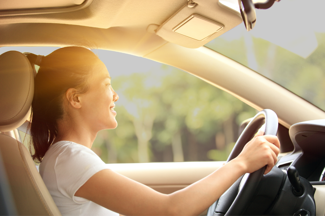 A woman is driving a car on a sunny day.