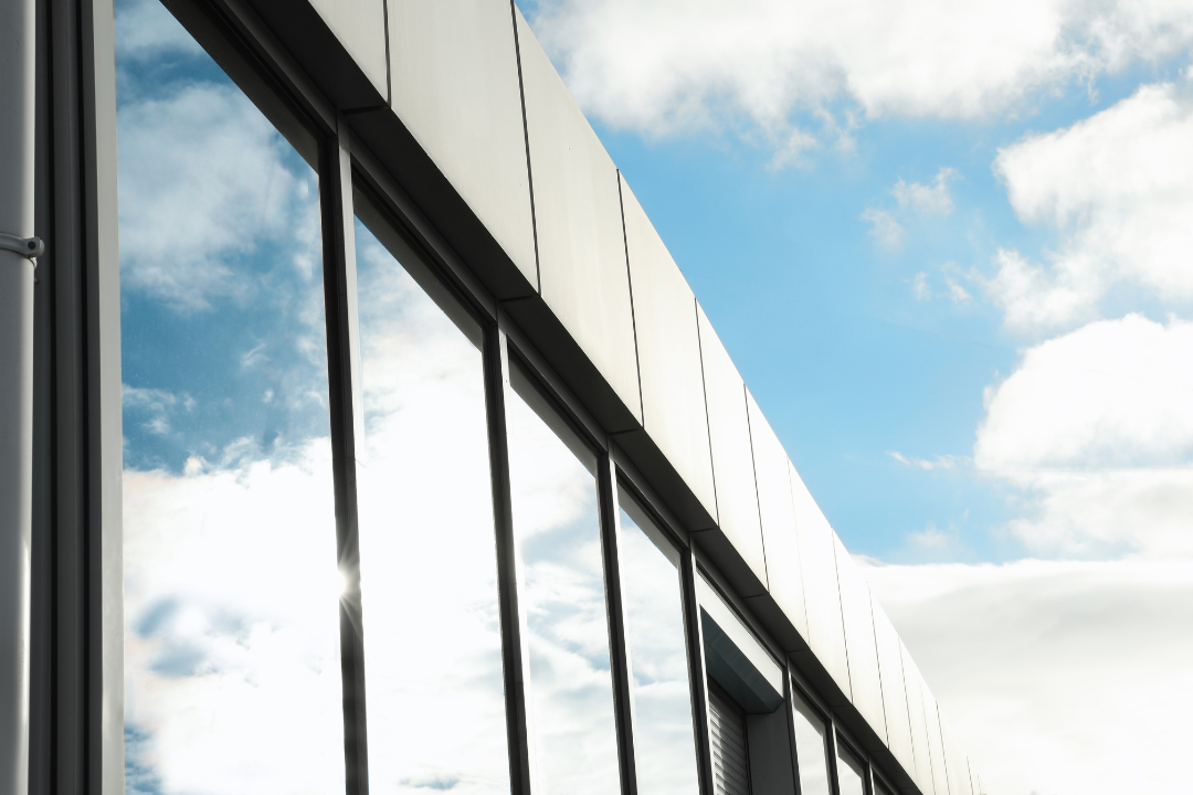 A building with windows reflecting a blue sky and clouds, featuring privacy film, located in San Antonio.