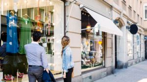 A man and a woman are looking at clothes in a store window.