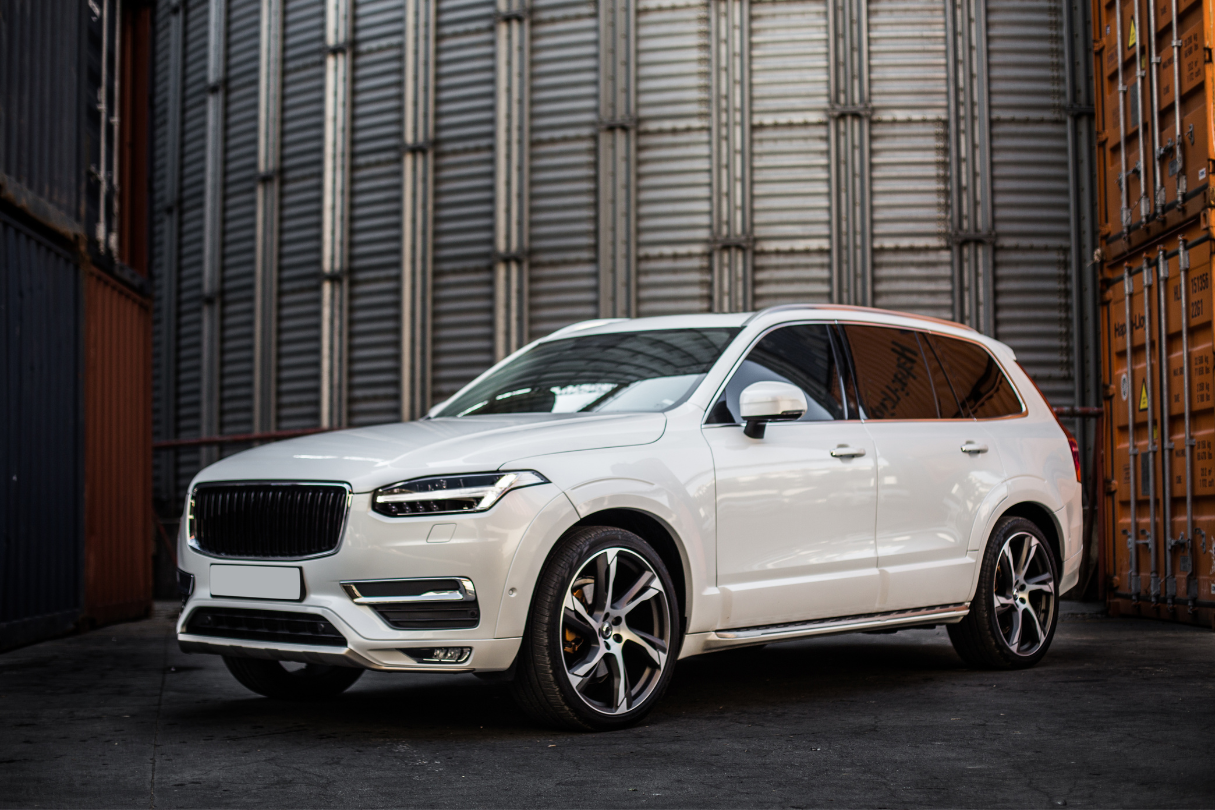 A white volvo xc90 is parked in front of a building.