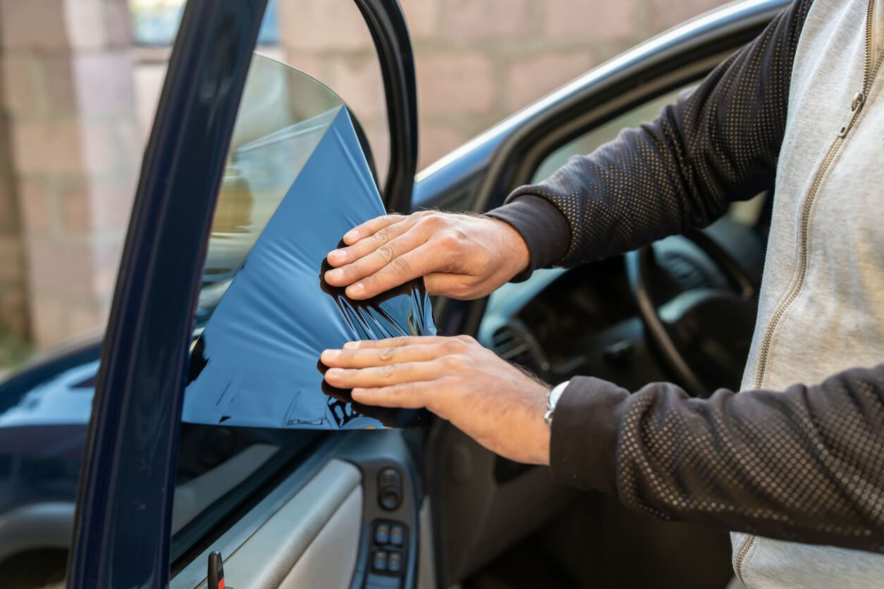 A man works on a car window, demonstrating a step in the window tint removal process.