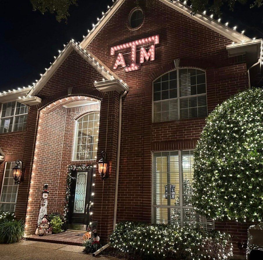 Brick home lit with warm white bulbs, wrapped shrubs and a lit sign