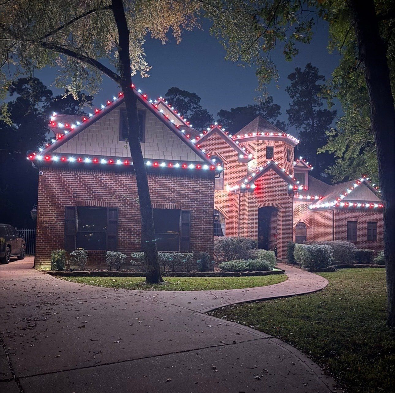 Red and white C9 bulbs outlining the peaks of a brick home at dusk
