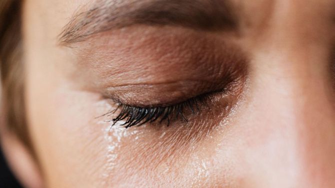 A close up of a woman 's eye with a tear coming out of it.