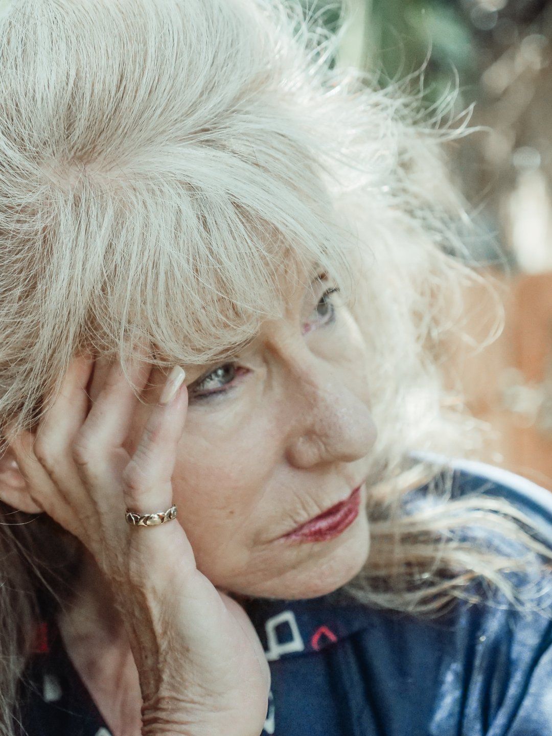 A woman with white hair is holding her head with her hand.
