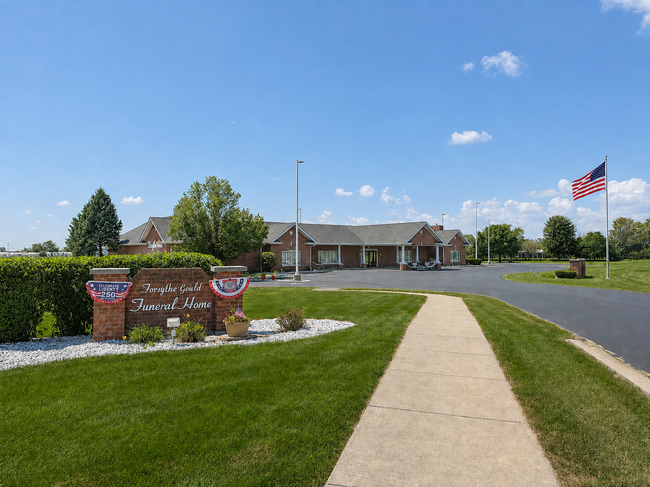 Suburban building with manicured lawn, sidewalk, flagpole, and patriotic sign under a blue sky
