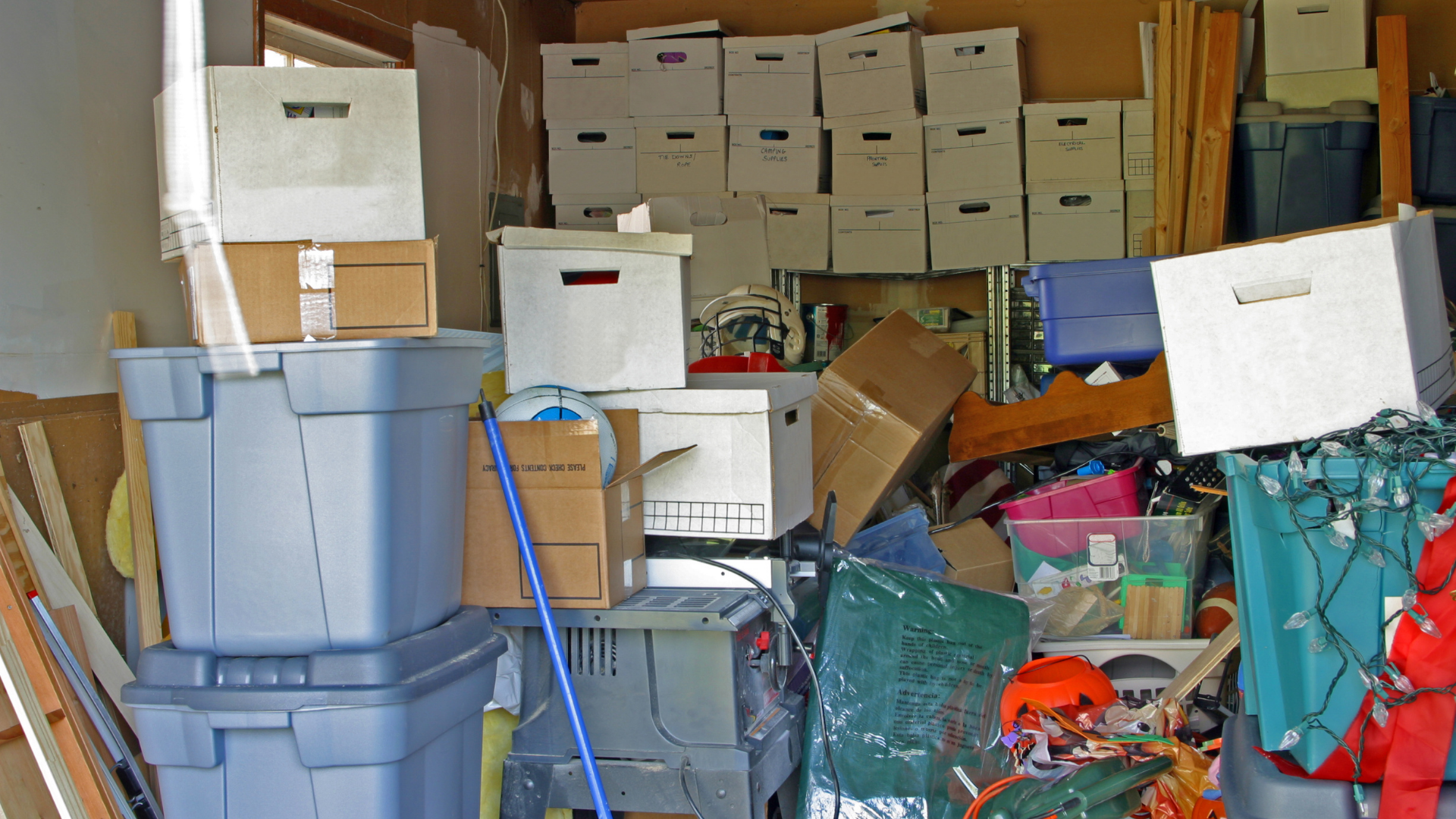 Cluttered storage room with boxes, bins, and various items piled high.