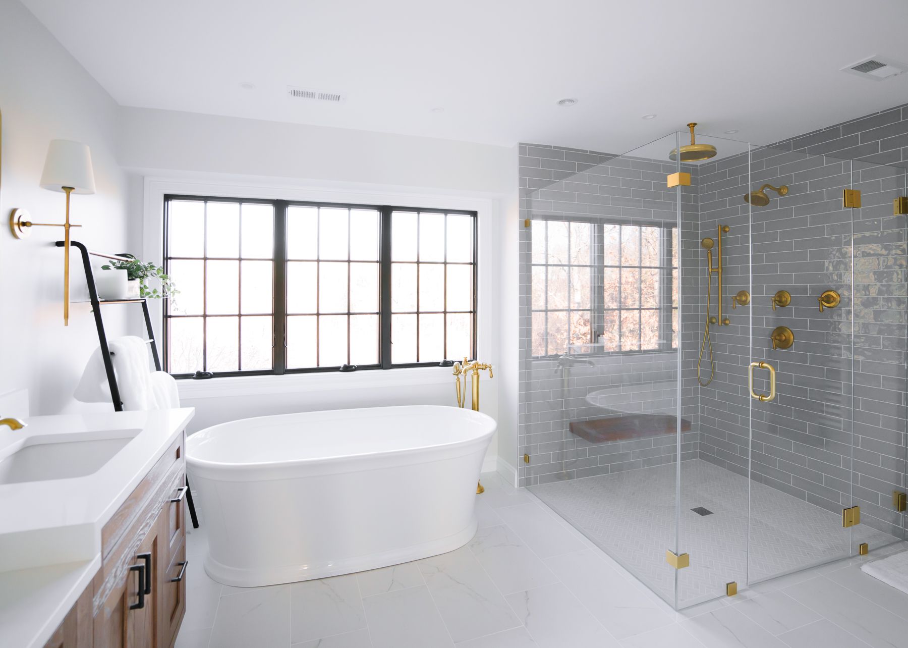 Bright white bathroom with a freestanding tub, double sink, and glass shower with gold fixtures