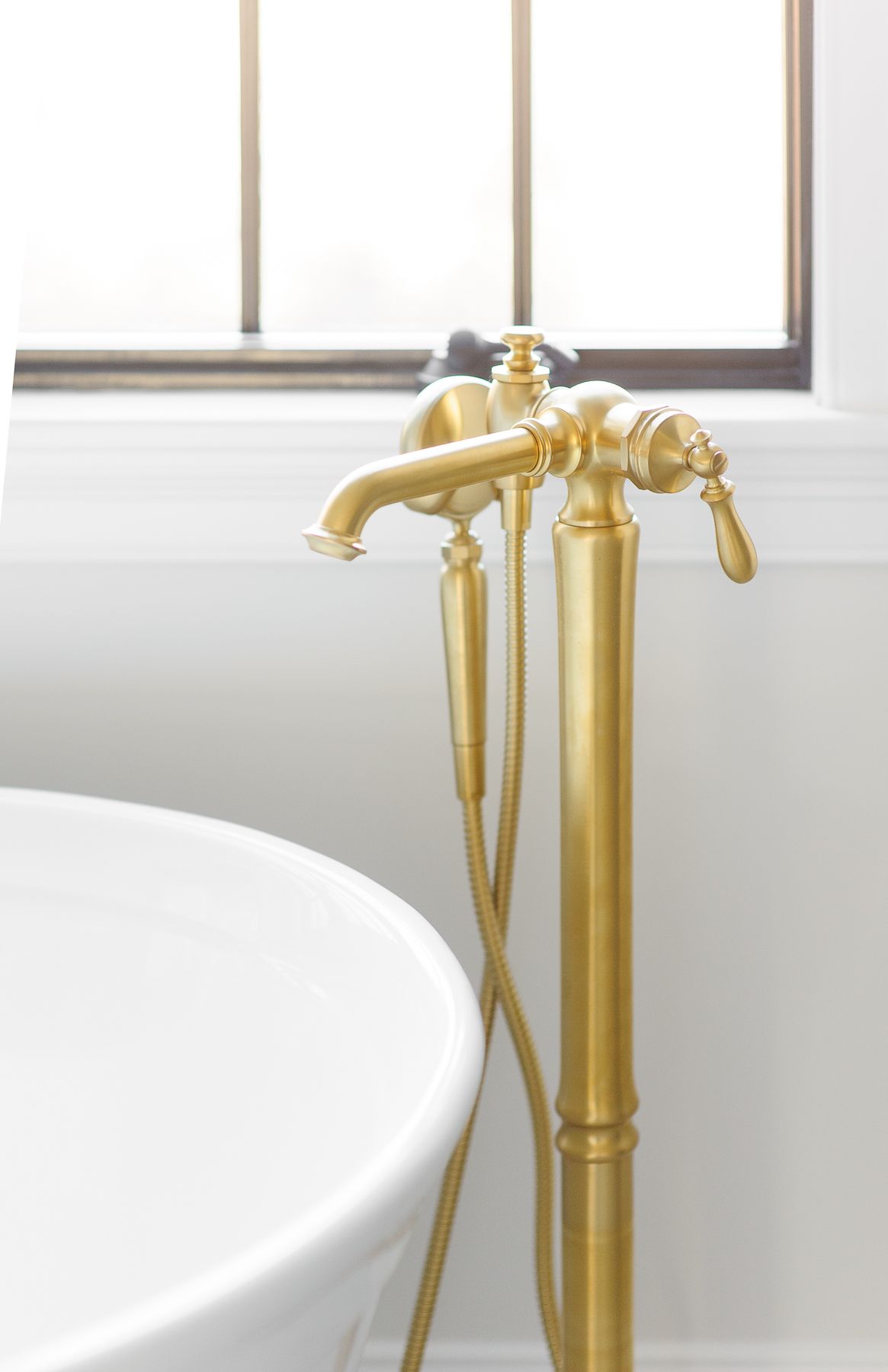 Brass vintage-style bathtub faucet beside a white tub by a window