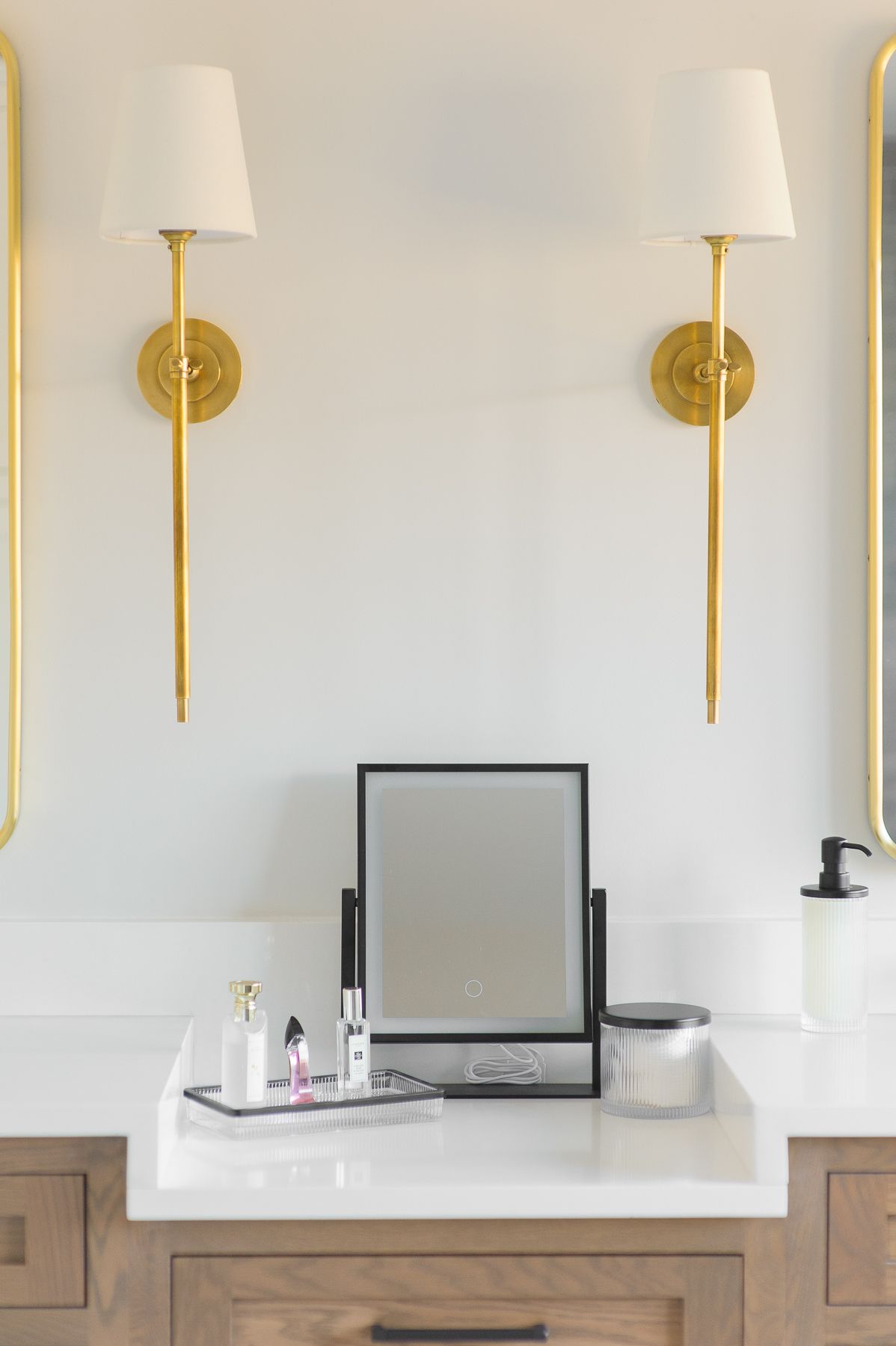 Modern vanity with white countertop, gold wall sconces, black-framed mirror, and toiletries.