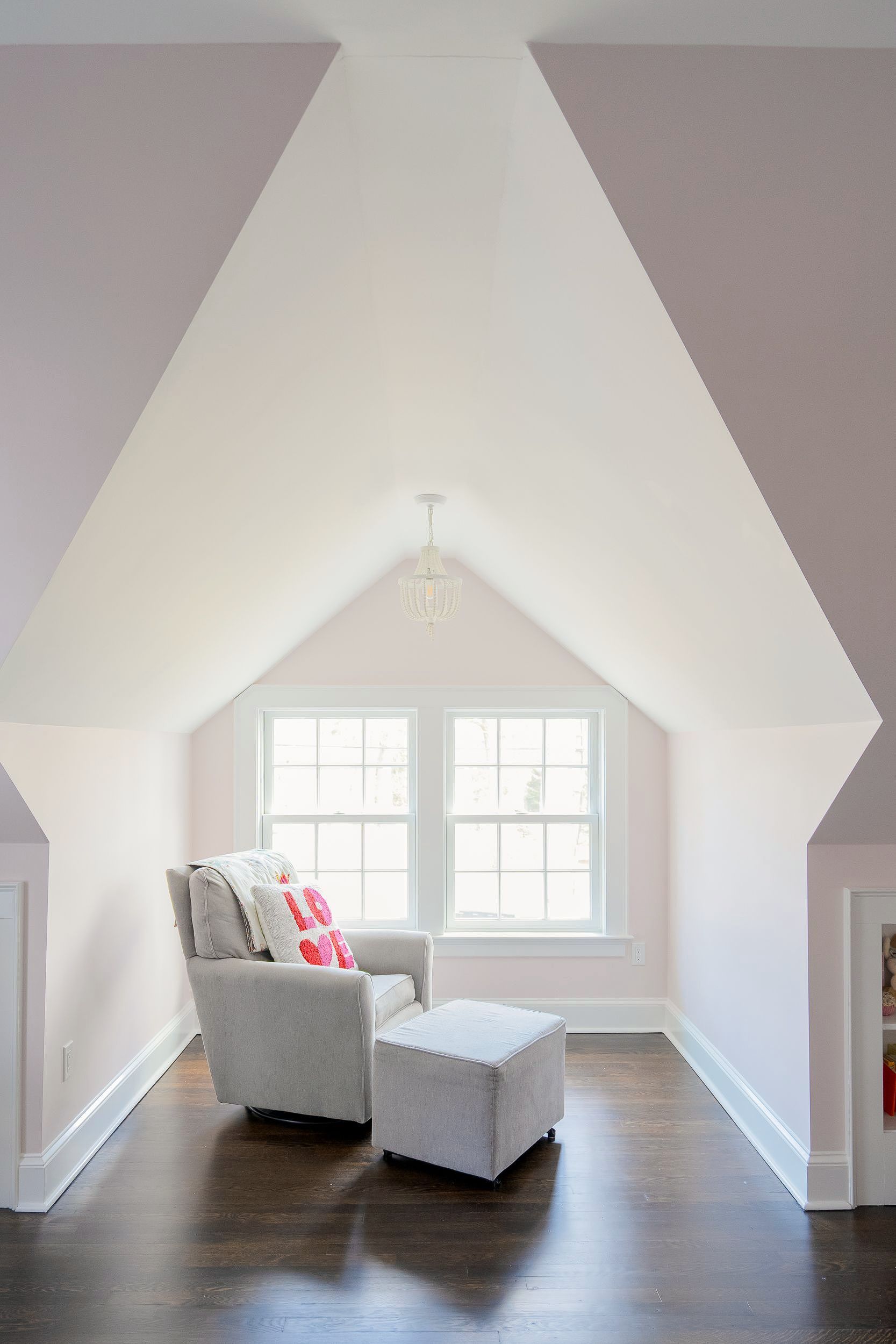 Bright attic sitting room with white walls, a large window, and a gray chair with an ottoman.