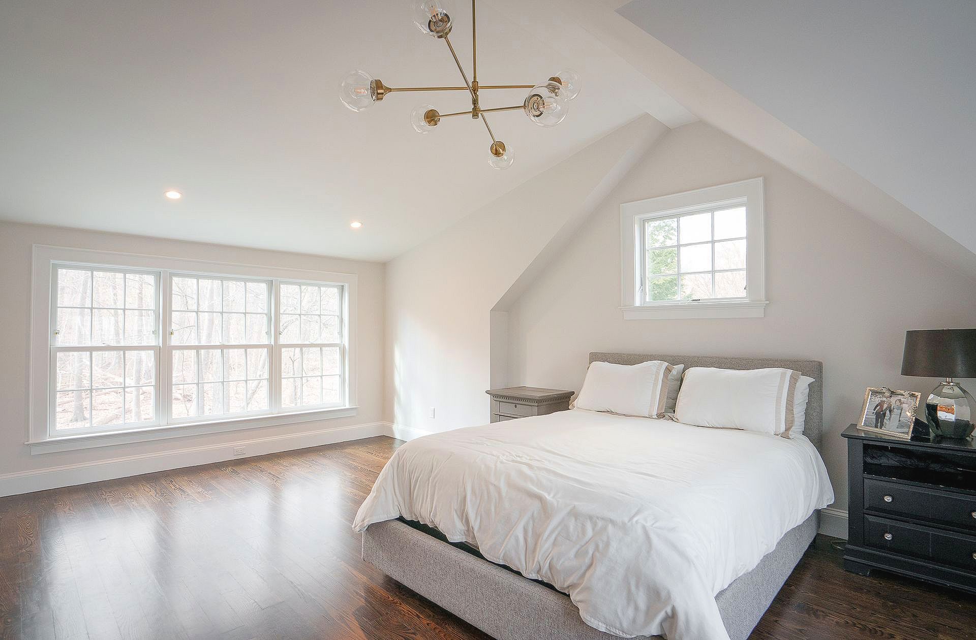 Bright bedroom with vaulted ceiling, large windows, white bedding, and dark hardwood floors