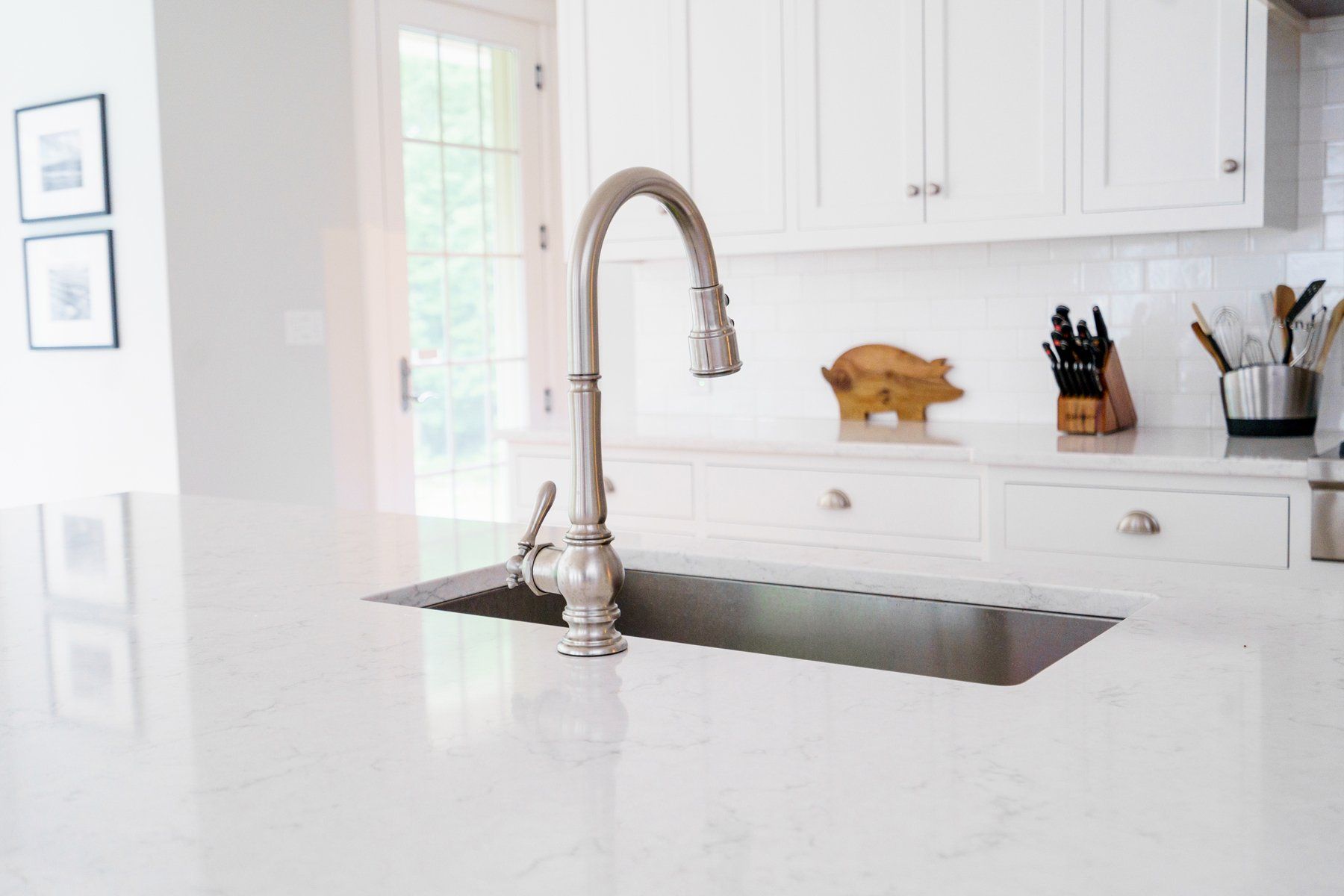Bright white kitchen with a stainless faucet over a marble island and white cabinets.