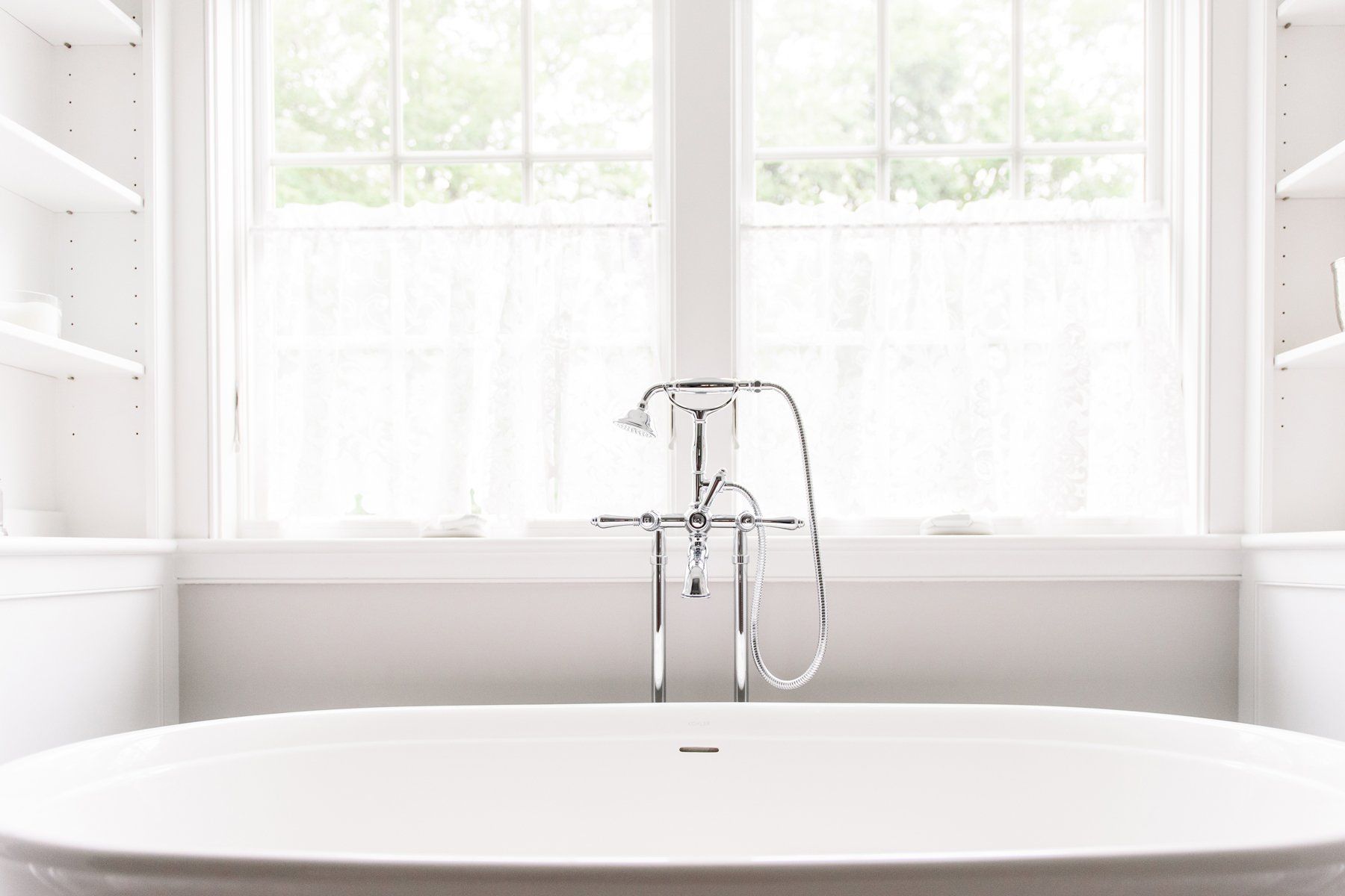 Bright minimalist bathroom with a freestanding tub and chrome faucet beneath a sunlit window