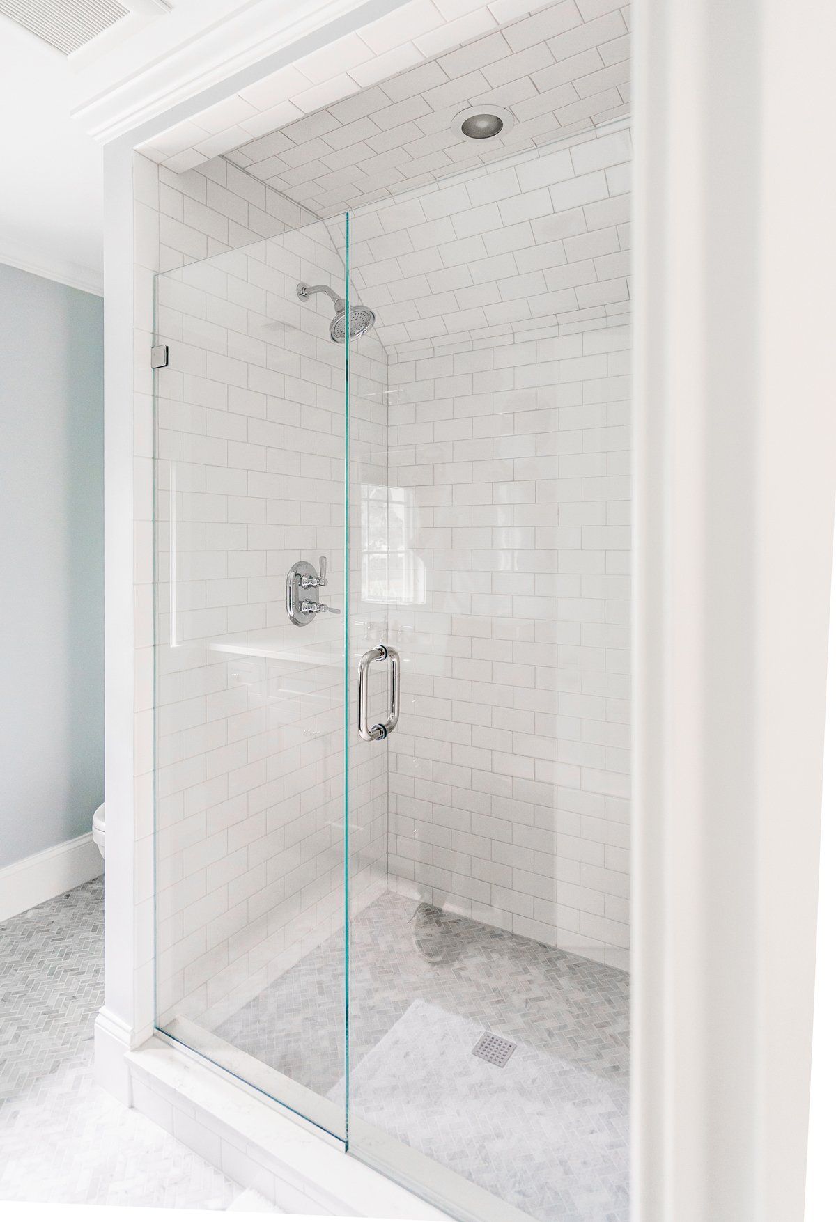 Glass-enclosed white tiled shower with chrome fixtures in a bright bathroom