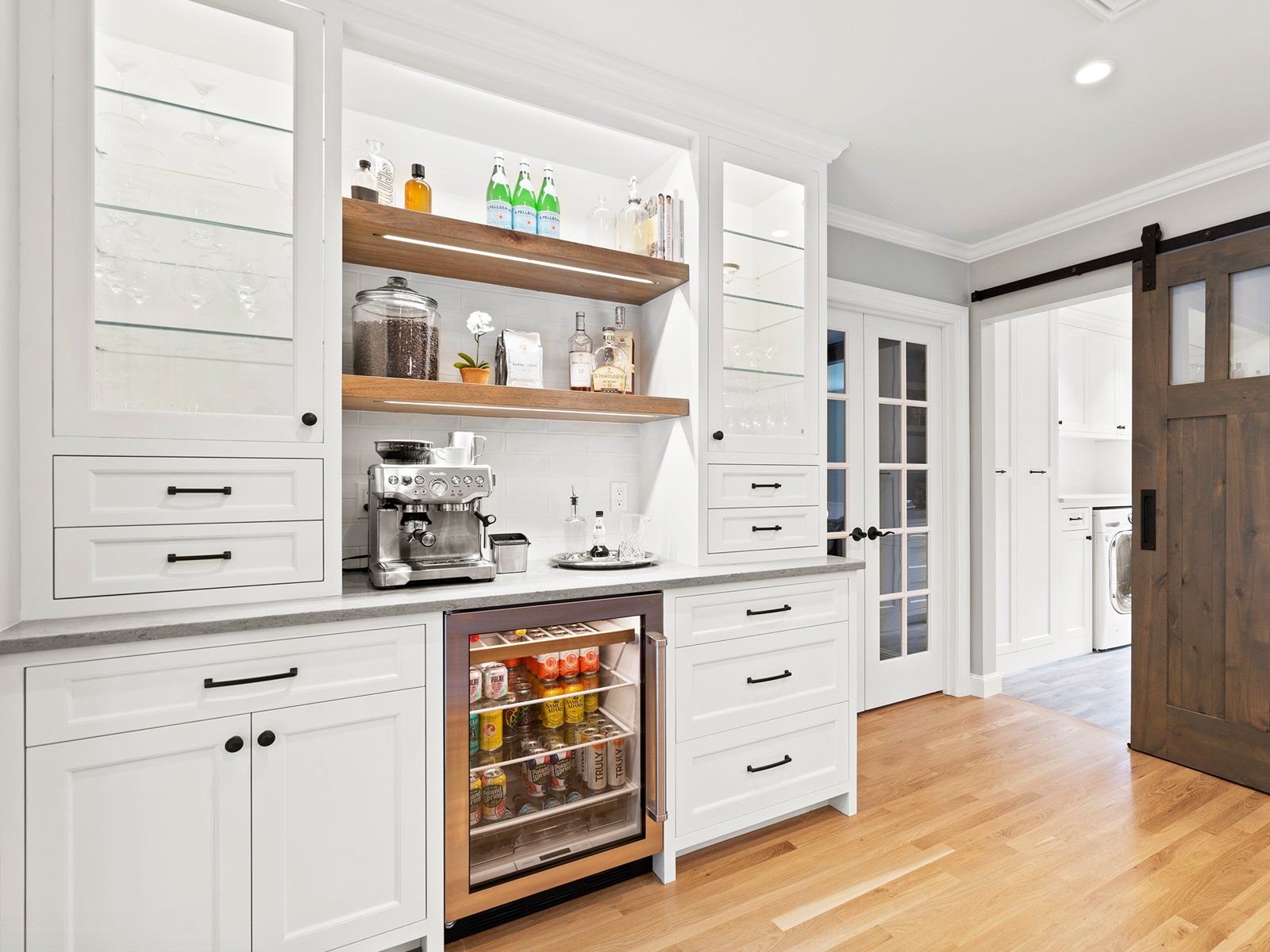 Bright white kitchen nook with open shelves, coffee machine, beverage fridge, and wood floor
