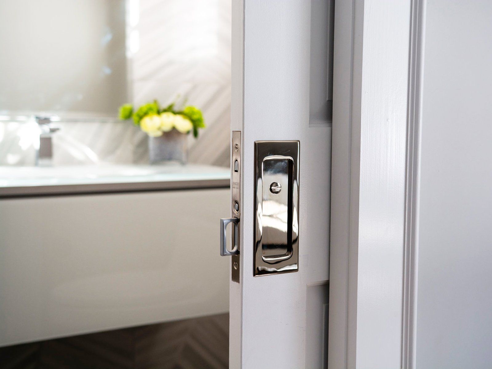 Close-up of a bathroom door latch with a blurred sink and yellow flowers in the background