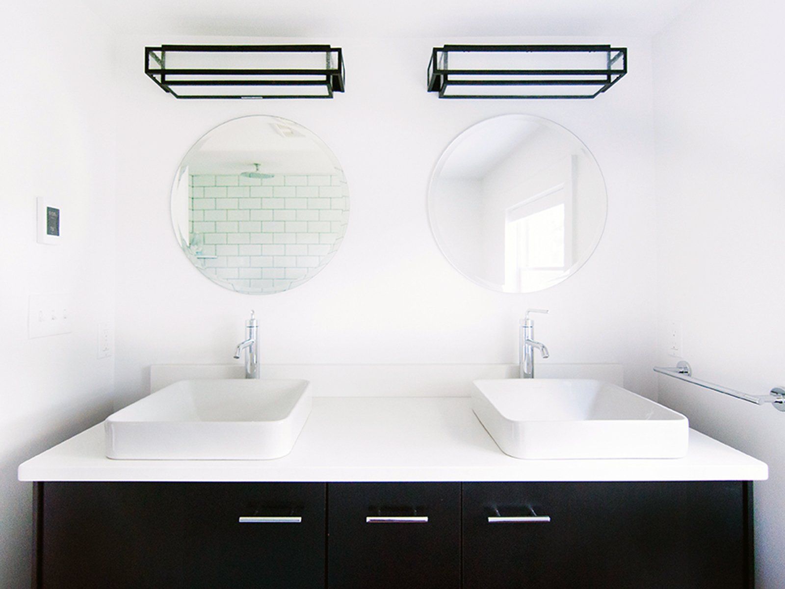 Modern white bathroom with double sinks, round mirrors, and black vanity cabinets