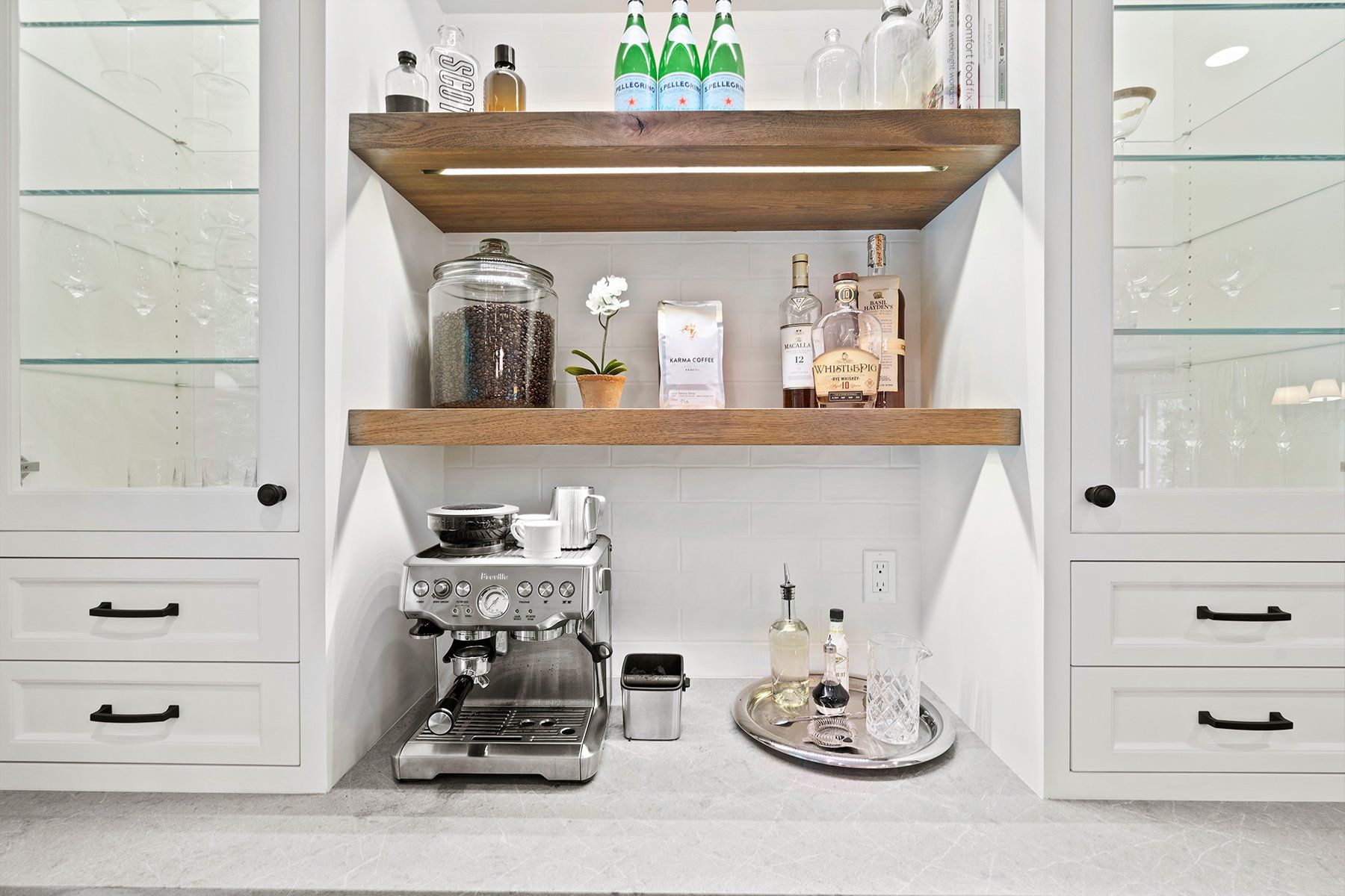 White built-in coffee bar with shelves, espresso machine, jars, and bottles in a bright kitchen nook
