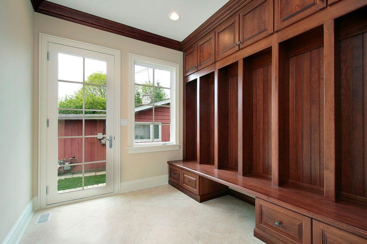 Empty walk-in closet with dark wood built-in cabinets, window, and glass door to a backyard.