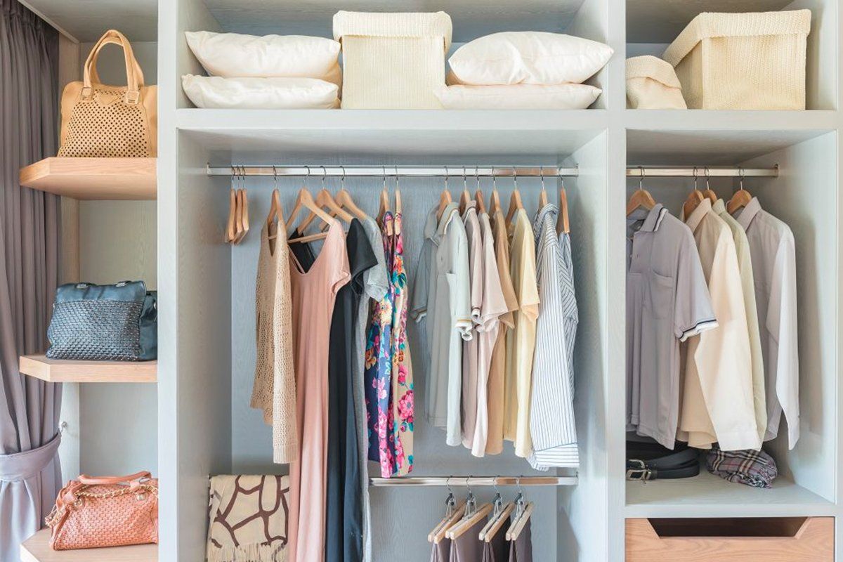 Open closet with neatly arranged clothes, shelves, baskets, and handbags in a light-colored wardrobe