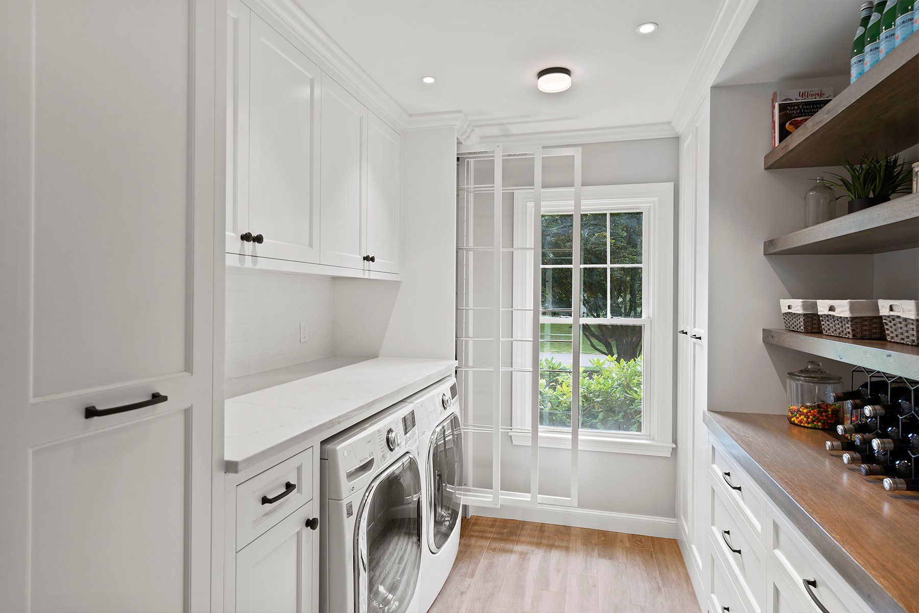 Bright white laundry room with washer, cabinets, shelves, and a glass door to a green garden.