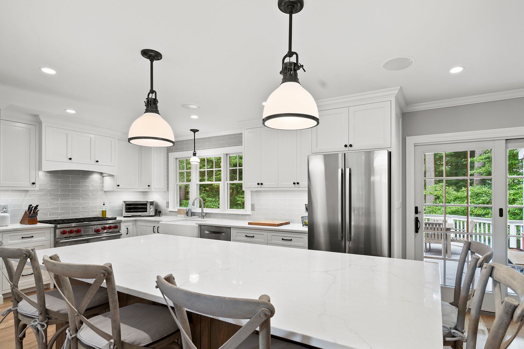 Bright white modern kitchen with island, pendant lights, stainless steel fridge, and large windows