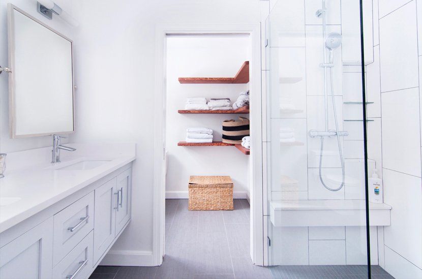 Bright white bathroom with vanity, mirror, shower, and open shelving with towels and a basket.