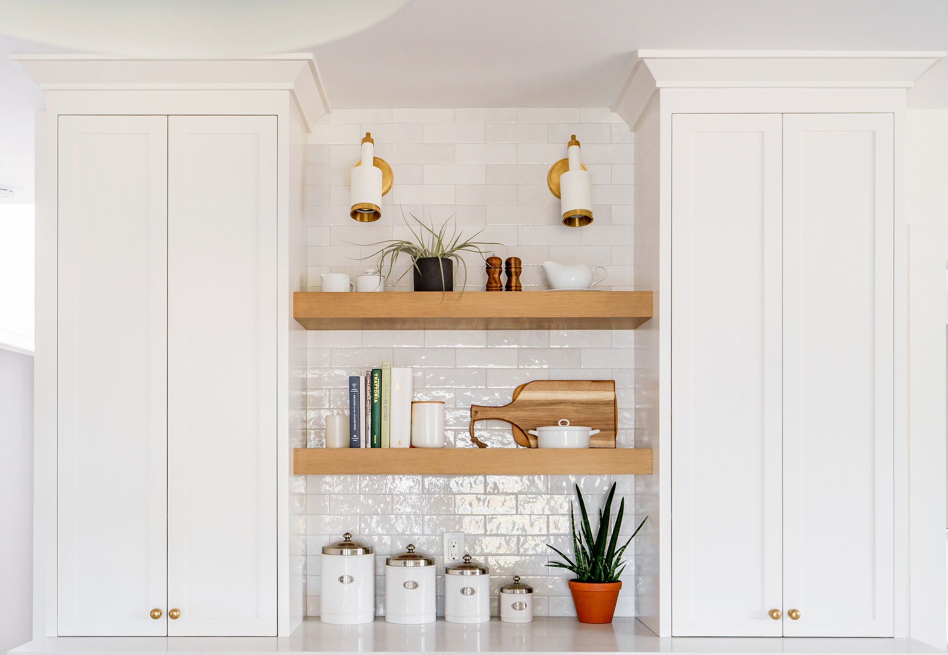 White built-in cabinets with wooden shelves, decor, and plants in a bright kitchen nook