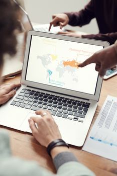 Personas señalando una computadora portátil que muestra un mapa del mundo sobre un escritorio.