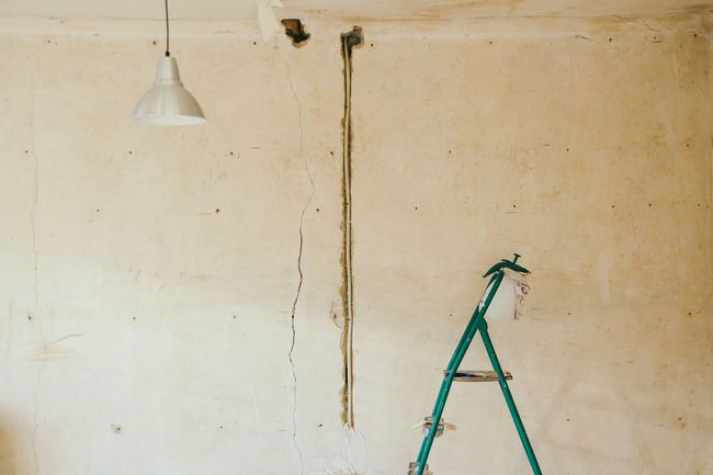 Bare room with cracked wall and ladder, ready for renovation